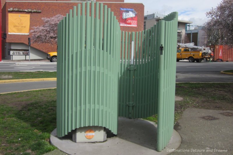 Open-air but private public urinal is a green-painted structure that looks like a curving thicket of metal poles