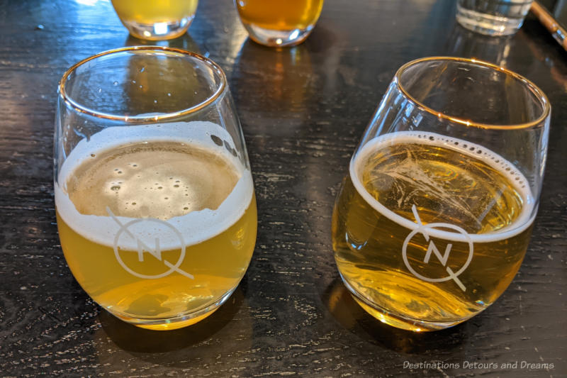 Two small glasses with the Nonsuch Brewing Co. logo containing light-coloured  beer