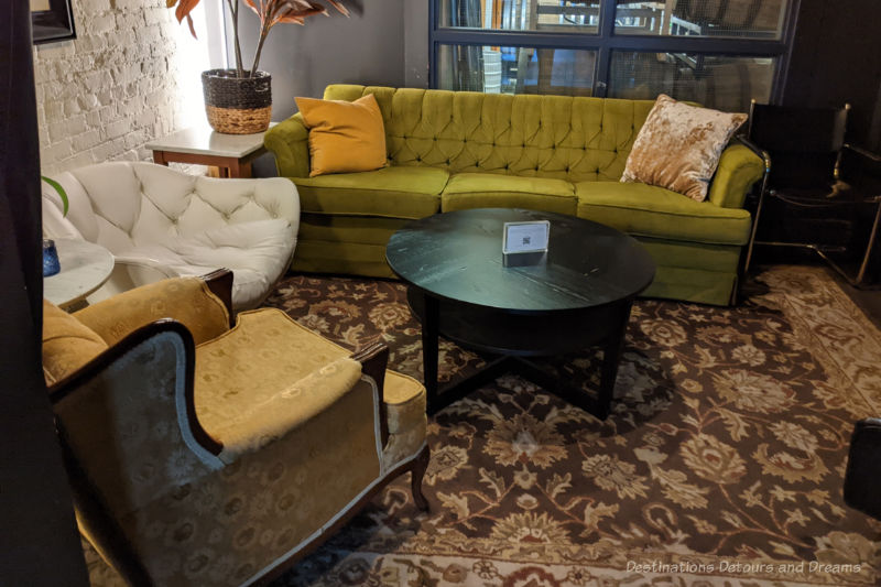 A cosy seating nook with a traditional green sofa, white basket-style chair, tradition arm chair, and round black coffee table