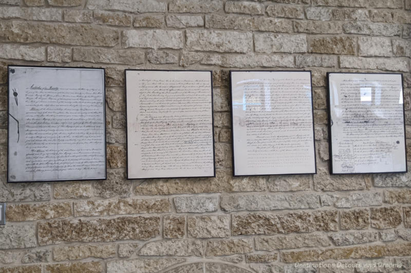 Four framed written pages of Treaty 1 hanging on a brick wall