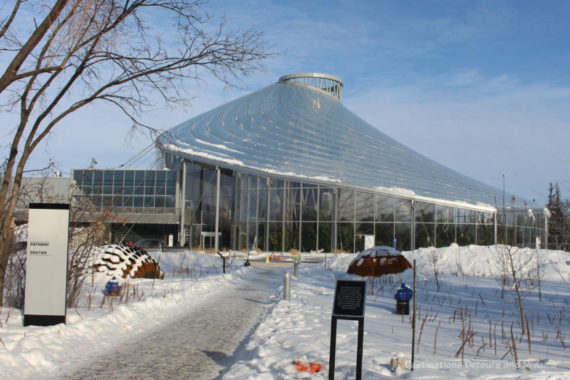 Exterior of The Leaf tropical conservatory with glass walls and translucent roof curving around and up on a winter day with snow around it