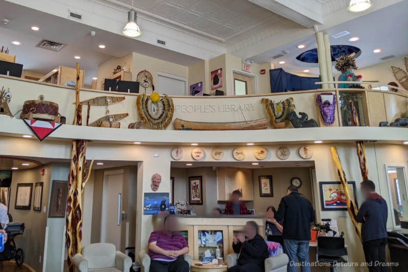 Curved almond-coloured wall with ledge below mezzanine floor covered with Indigenous art and artifacts