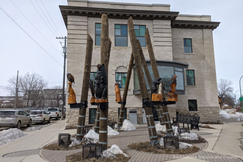 Manitoba Indigenous Cultural Education Centre three-story brick building with sculpture of a circle of seven tall pole each with a carved animal on it in front of the building