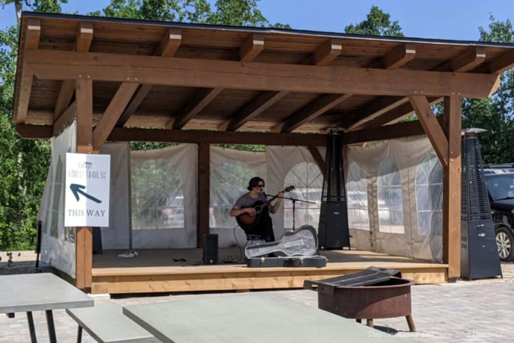 Man with guitar playing on open-air covered wood stage with tenting on three sides