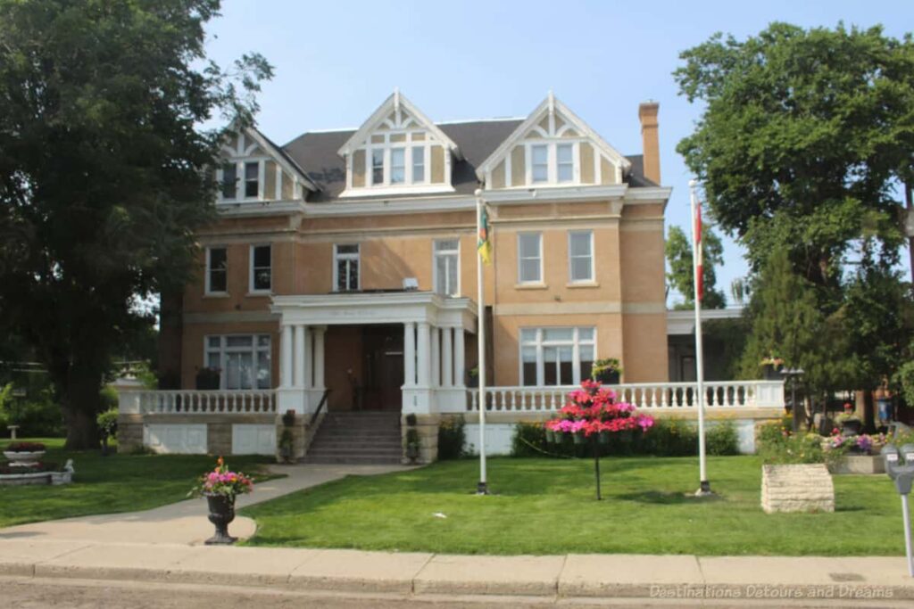 Historic light coloured stone three-story house with white trim, large veranda, and white pillars holding up awning over entryway