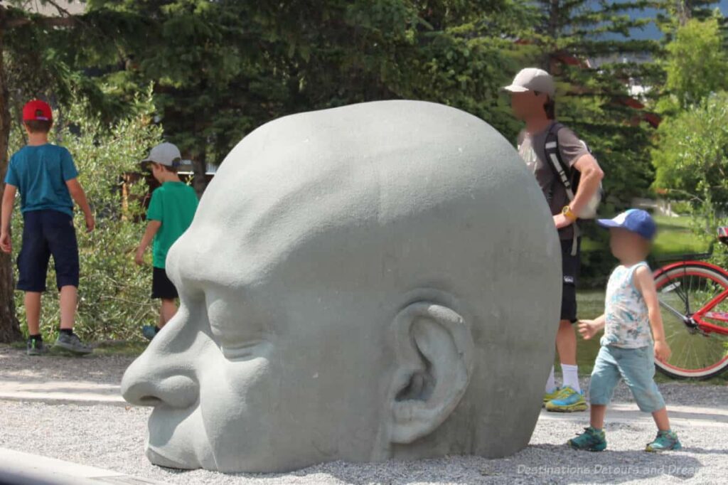 Sculpture of a grey head from the mouth up with the rest of it appearing to be below ground