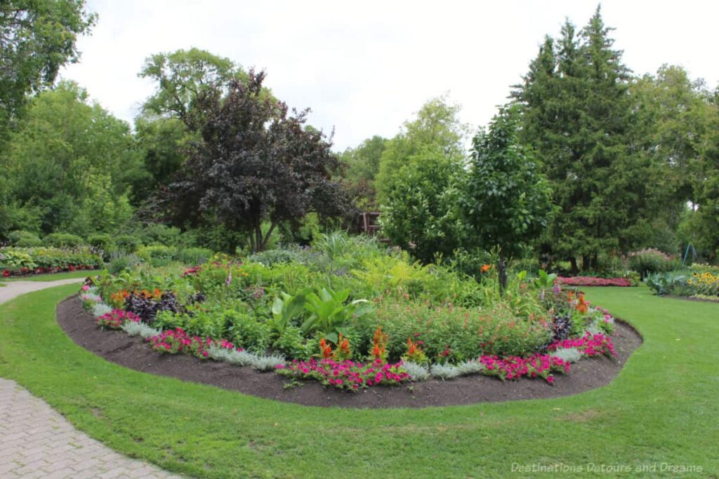 Circular flower bed containing greenery in the middle bordered by pick and orange flowers