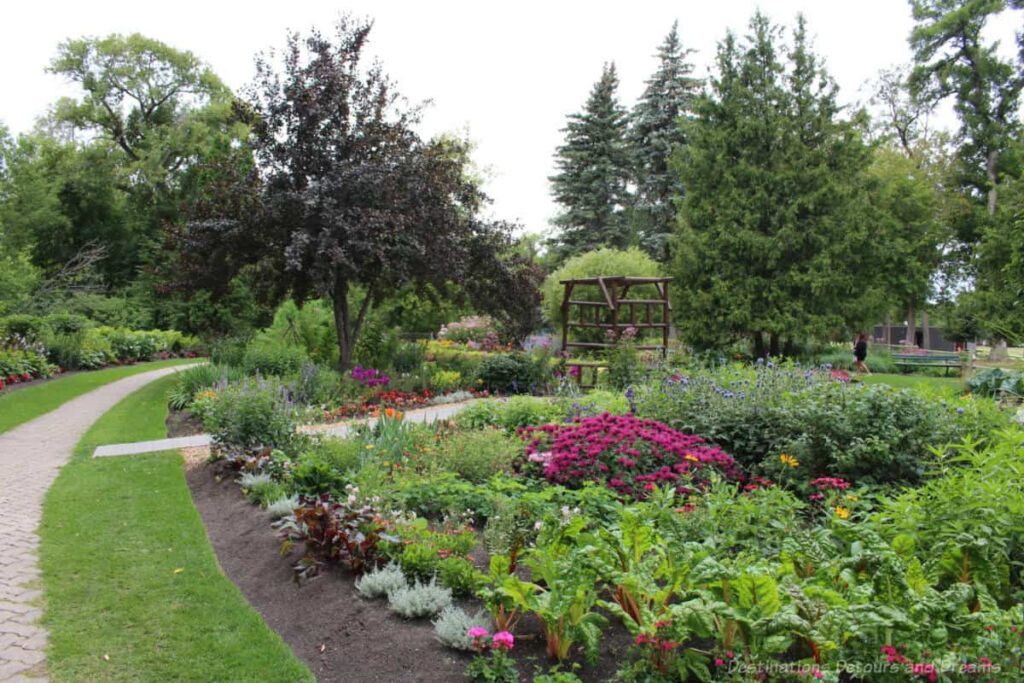 Flower bed with a variety of colours, surrounded a path and tree, with a wooden trellis in middle