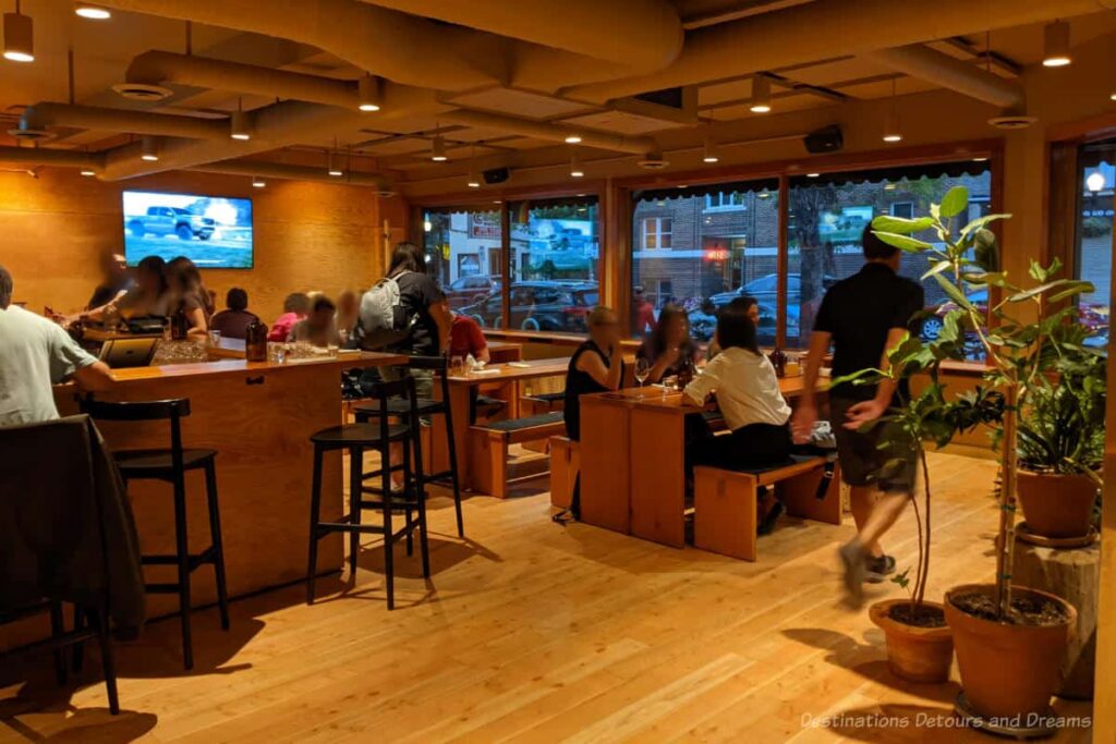 Bar and table and bench seating in a taproom and restaurant with windows to street