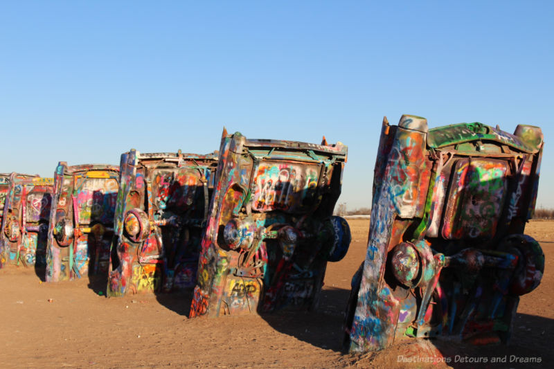 Bodies of old Cadillac car son end with one end partially buried and the remaining portion spray painted many colours at Cadillac Ranch