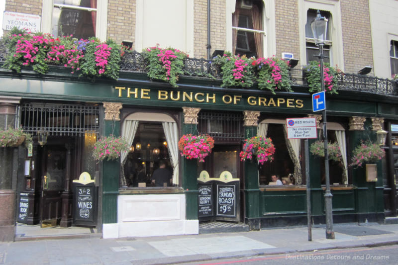 Exterior of the The Bunch of Grapes pub in London with flower pots of pink flowers cascading from second level