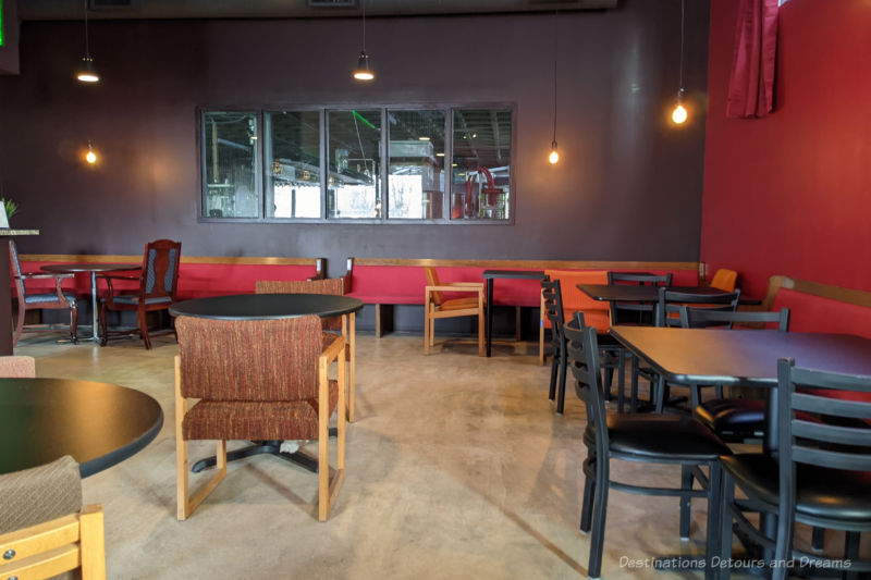 Tables in a fairly plain wine tasting room with window into brewing area