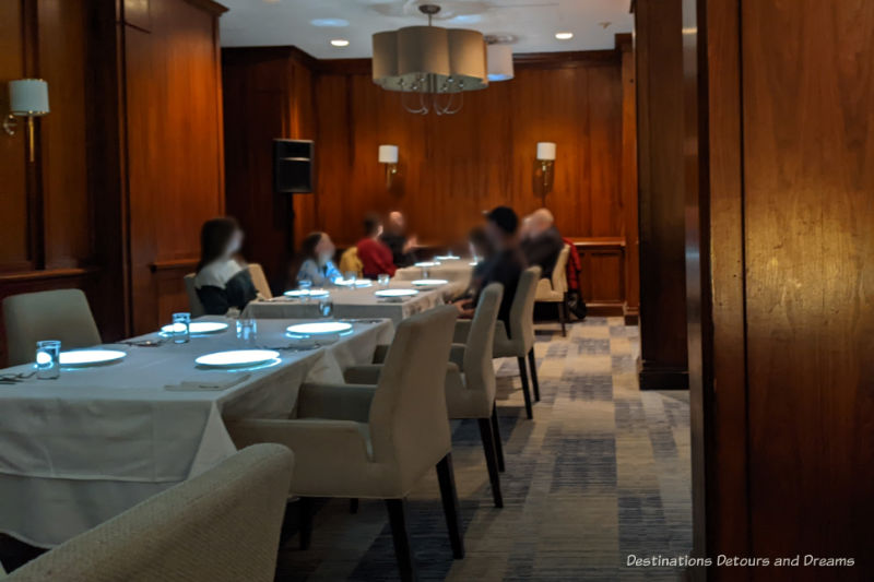 Le Petit Chef The Velvet Glove Wood-paneled restaurant with tables covered in white table clothes and white upholstered chairs
