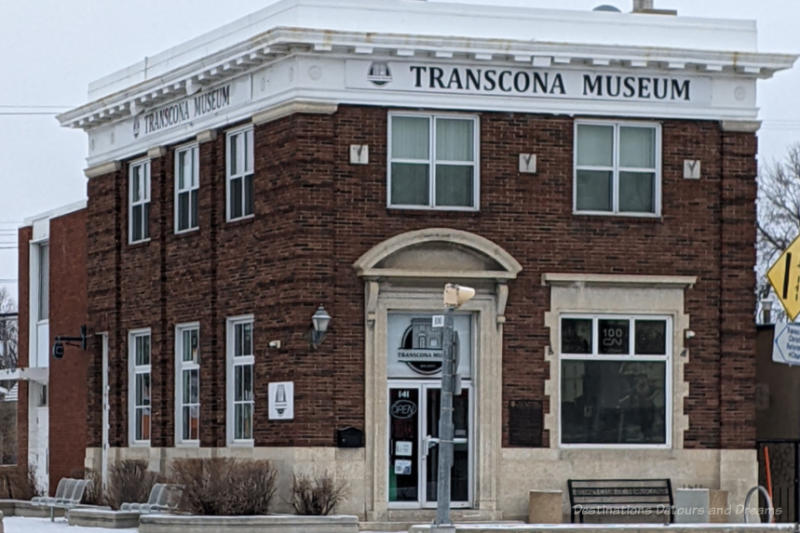 TransconaMuseum Two story dark brick building with white trim along roofline, lighter coloured stone around doorway and at base with TRANSCONA MUSEUM written on the white trim