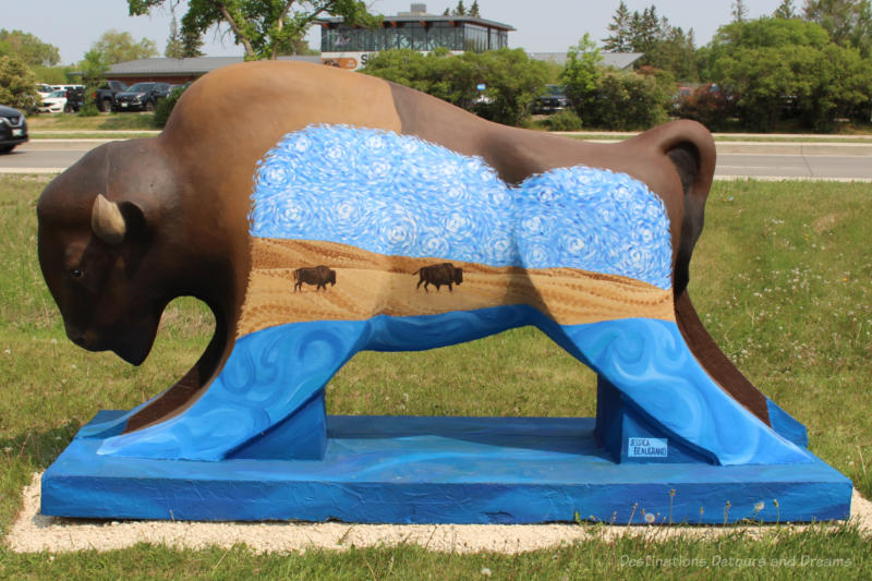 Bison on the Boulevard What Is What Was Brown concrete bison with a blue base and legs, a prairie scene painted on side showing a couple of bison running across prairie