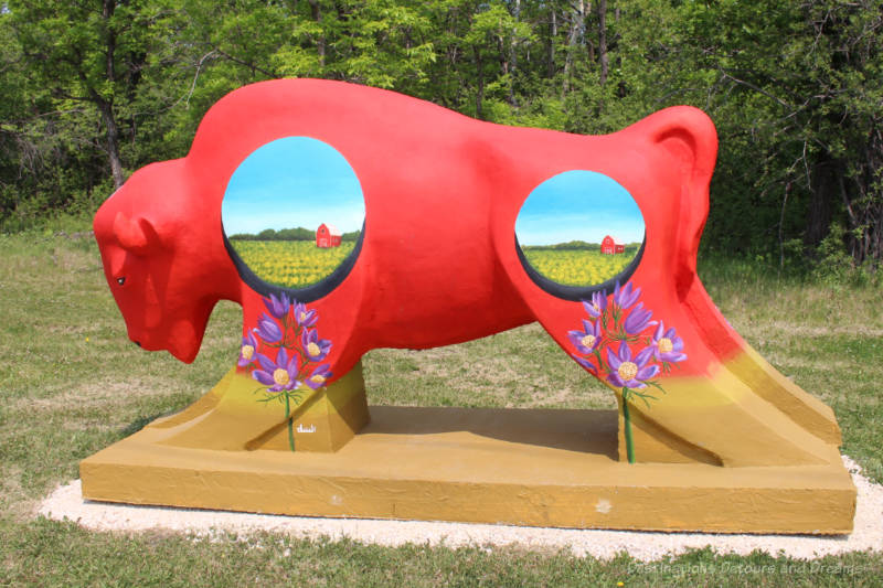 Bison on the Boulevard Praire Appa A red concrete bison contains two circle paintings on its side of a prairie field and barn and crocuses on its legs