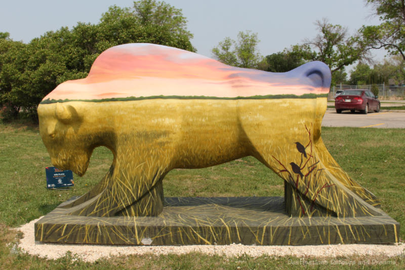 Bison on the Boulevard Wild Prairie Bottom half of concrete bison painted to reflect golden wheat fields and top half in shades of pink and blue to reflect the sky