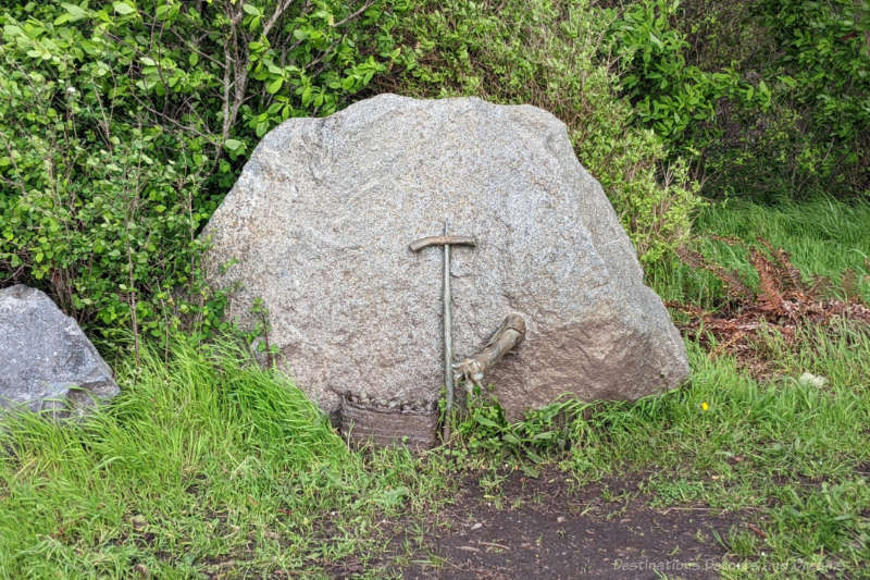 Sculpture on the side of a rock in a park shows a hand holding a digging tool and a basket at the base