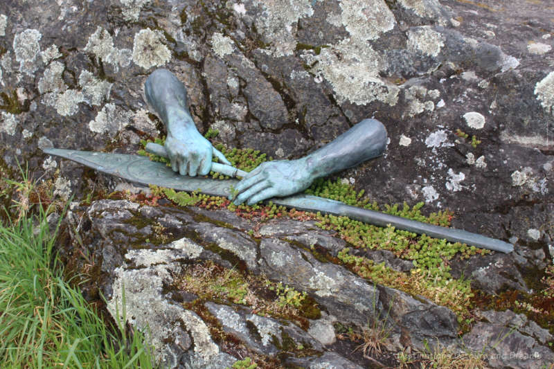 Bronze sculpture of hands protruding from a rock and holding a canoe paddle