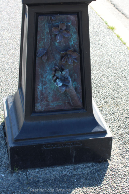 Sculpture on the side of the bottom part of a street lamp features hands holding dogwood blossoms