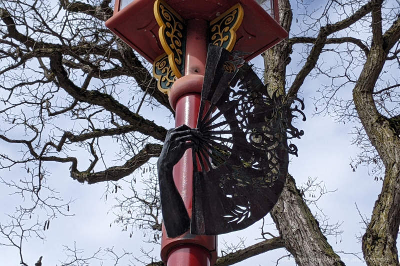 Bronze sculpture of a hand holding a Chinese fan wrapped around a red streetlamp