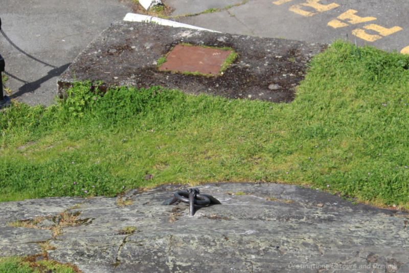 looking down at a rock at the edge of a parking lot with a bronze sculpture in the rock showing hands tying a rope to a mooring ring