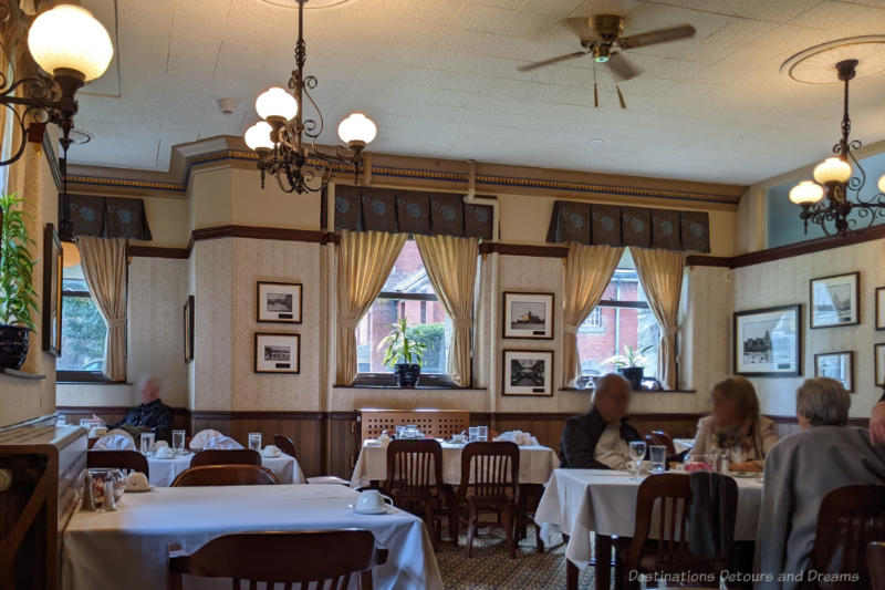 White tablecoth-covered tables in a restaurant with wallpapered walls and wood accents