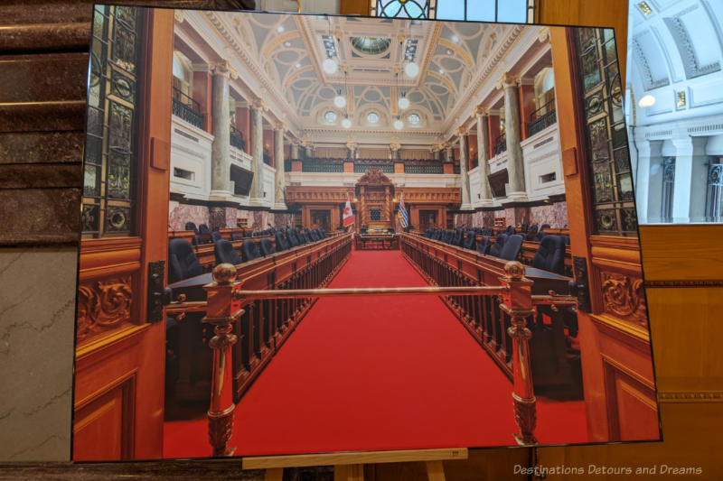 Photo showing a legislative assembly room with red carpet, seats behind wooden railings and ornate pillars and ceeiling