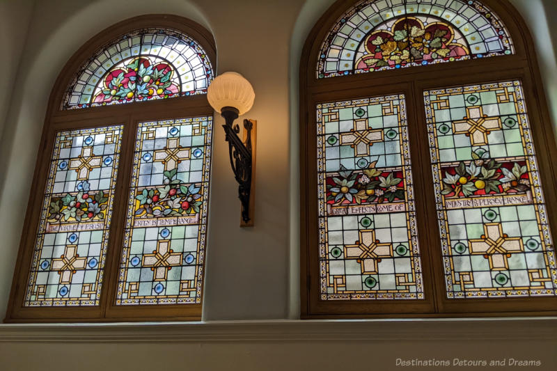 Two stained glass windows separated by small area of wall with sconce on it