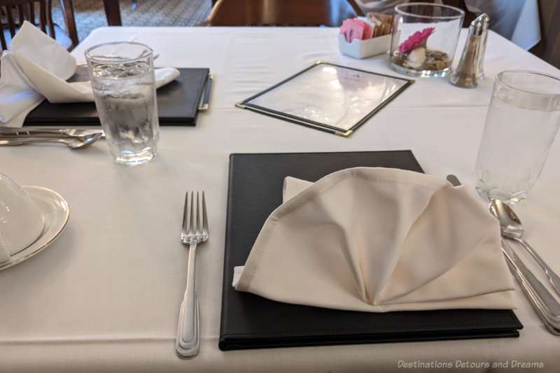 Dining table covering with white tablecloth and two place settings with menus and folded napkins