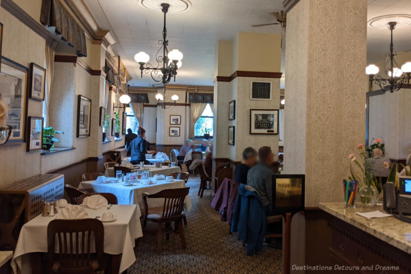 Restaurant dining area with wallpapered walls, wood accents, and tables covered with white tablecloths