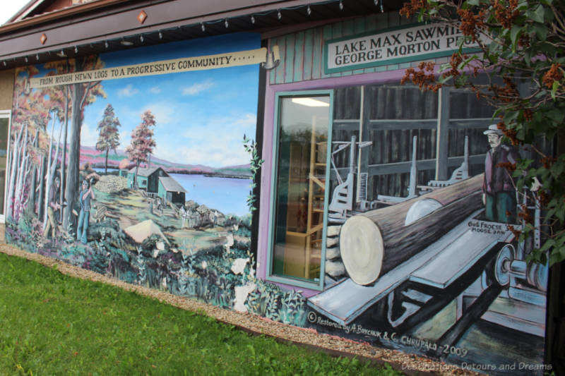 Boissevain Outdoor Art Gallery Morton Sawmill Mural on the outside of a building shows a log going through a blade at a sawmill on the right and a man felling a tree in woods alongside a lake on the left