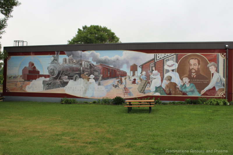 Boissevain Outdoor Art Gallery Mural on the outside of a building showing a train station in the late 1800s with people on the platform and a steam train approaching - part of Boissevain Outdoor Art Gallery