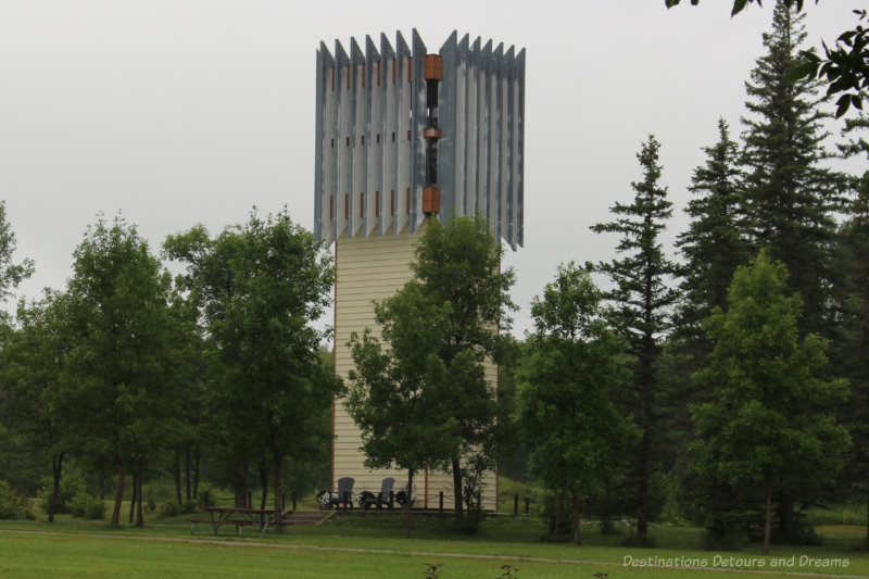 Bell tower with wood plank (light yellow colour) base and steel vertical bars at top