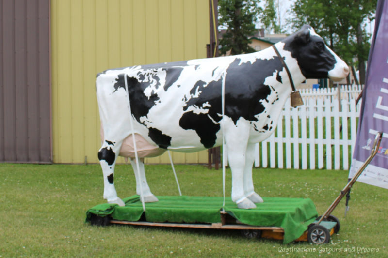 Statue of a white cow with black markings wearing a cowbell