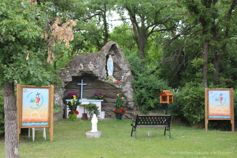 small grotto with altar in rock-like structure and statue of Mary in upper alcove surrounded by trees