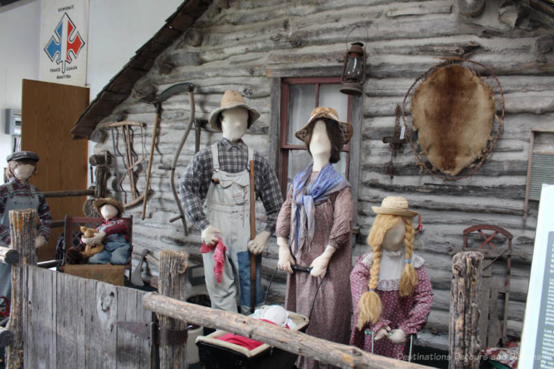 A life size diorama in a museum showing pioneers in front of a log house