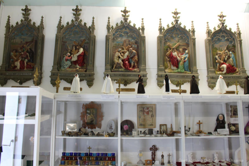 Row of religious sculpture paintings above a display case of assorted religious artifacts