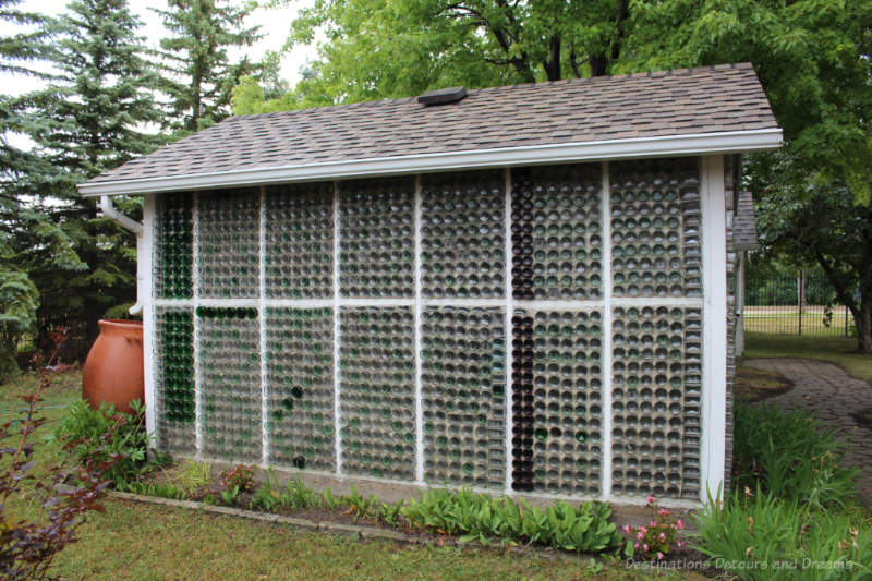 Wall of a glass bottle house showing wood framing, glass bottles encased in cement, and a shingled roof