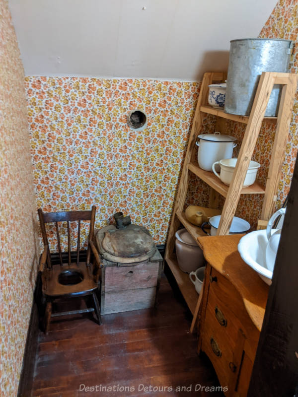 Miami Railway Station Museum Washroom Toilet room with yellow and orange flowered wallpaper circa early 1900s with shelves contain chamber pots and a wood framed toilet to be used only at night