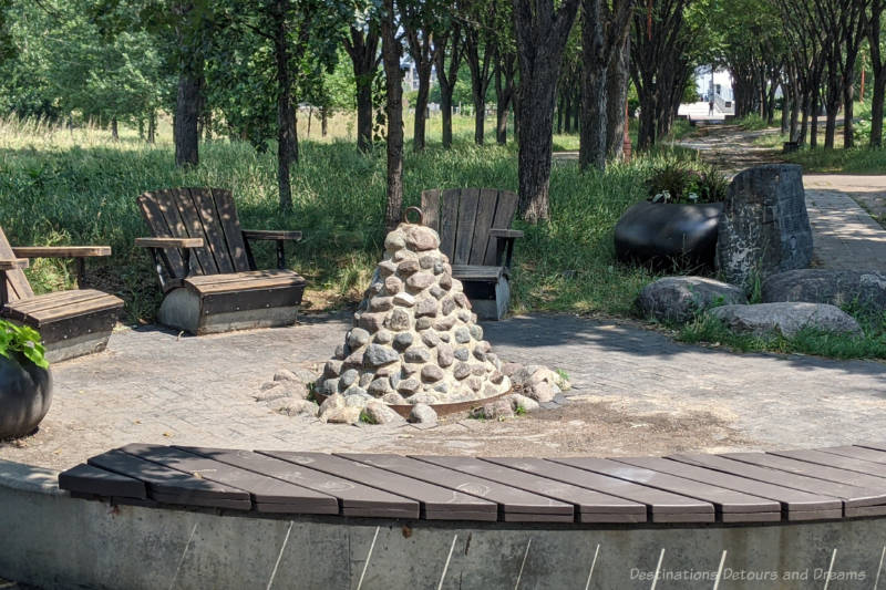 The Forks Turtle Tours Peace Meeting Site Circular bricked area in shaded area with wooden seating along outside and a stone monument resembling a fire pit in the centre