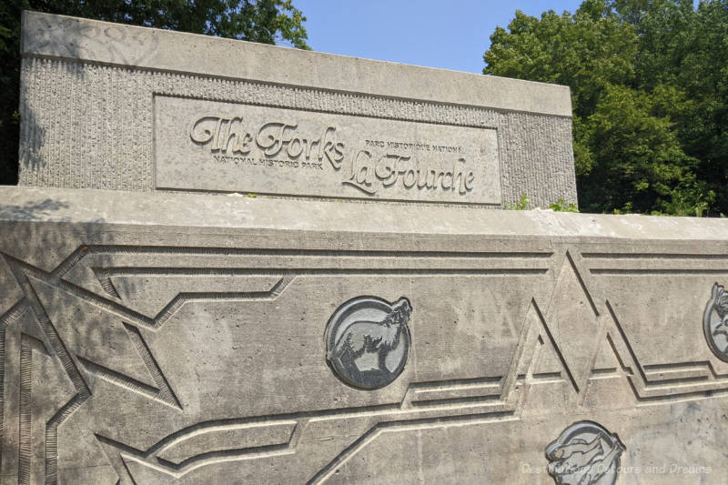 Stone wall with geometric design and animals etched into it as sign saying The Forks National Historic Site