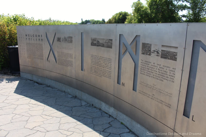Viking Park Culture Wall A curved stainless steel wall at the edge of an outdoor stone patio contains etched information