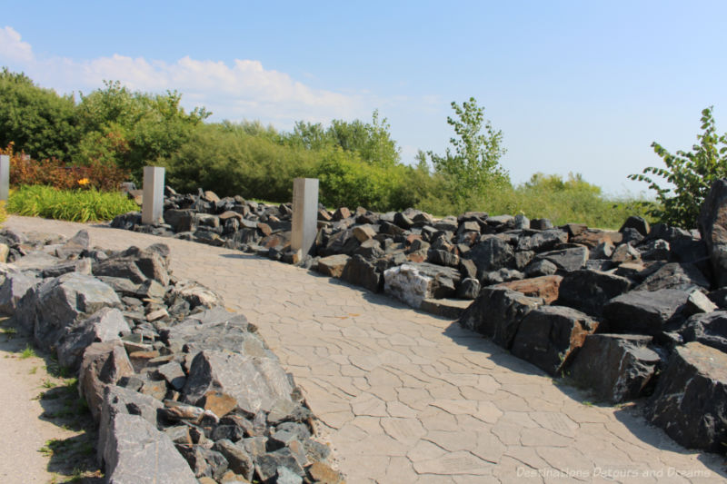 Viking Park Walkway Paving stone walkway bordered by dark rocks with greenery in background