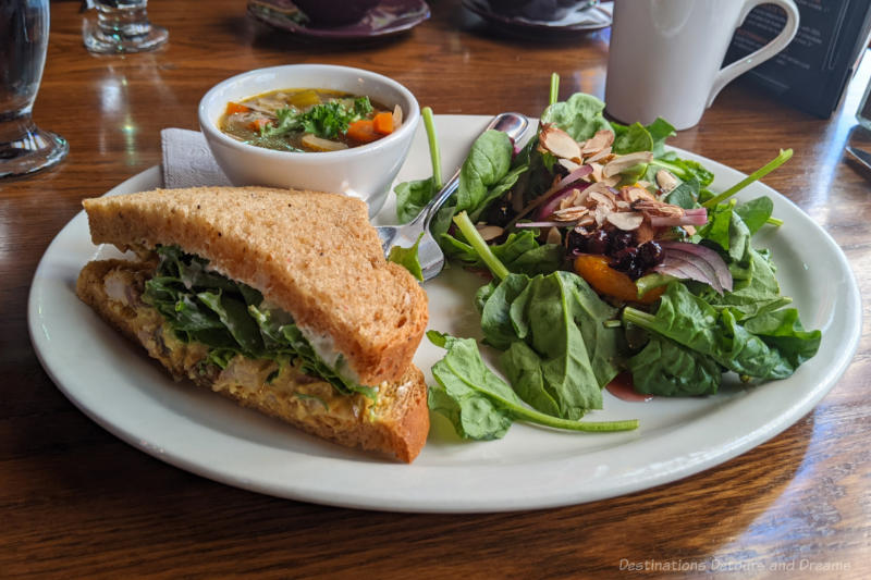 White plate containing spinach salad, half an egg salad sandwich and a small bowl of soup