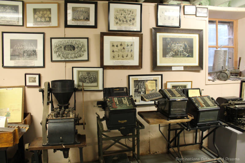 Daly House Museum Basement Museum display of adding machines and calculators with historical photos of team and groups on the wall