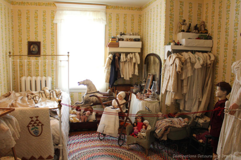 Daly House Museum Child Bedroom Victorian-era child's bedroom in a house museum features gold and green wallpaper, white metal frame bed, vintage clothing and toys