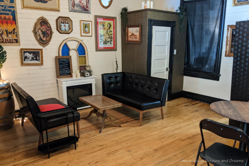 Rendezvous Eatery Back Area Back area of a taproom features a couple of sofas beside a portable fireplace, wood flooring, white brick wall covered with paintings and posters