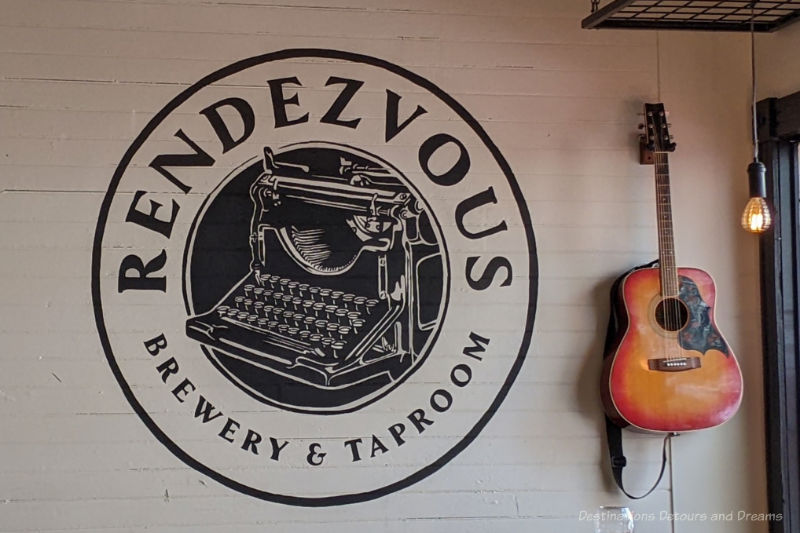 Rendezvous Guitar hanging on wall beside circular black and white painted sign with a typewriter in centre and Rendezvous Brewery & Taproom printed along outer ring