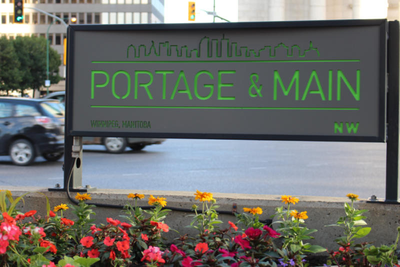 Portage & Main Barricade Concrete barrier with a street intersection sign and flowers planted